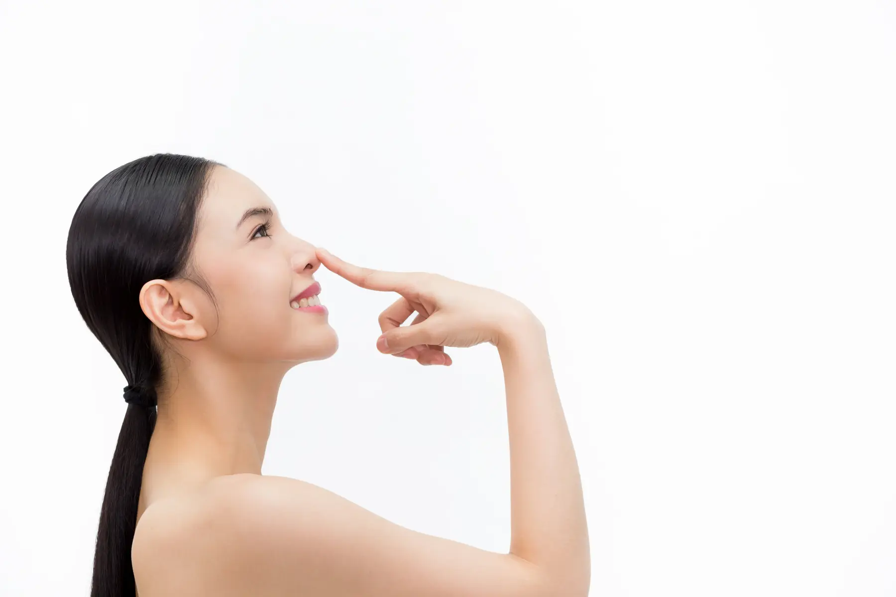 Rhinoplasty 1 Smiling woman touching her nose, highlighting facial profile and smooth skin.